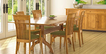 A wooden dining table with six matching chairs is centrally placed on a light-colored wood floor. The table holds a small bowl, and in the background, there's a wooden sideboard adorned with decorative items. Large glass doors allow natural light to enter the room.