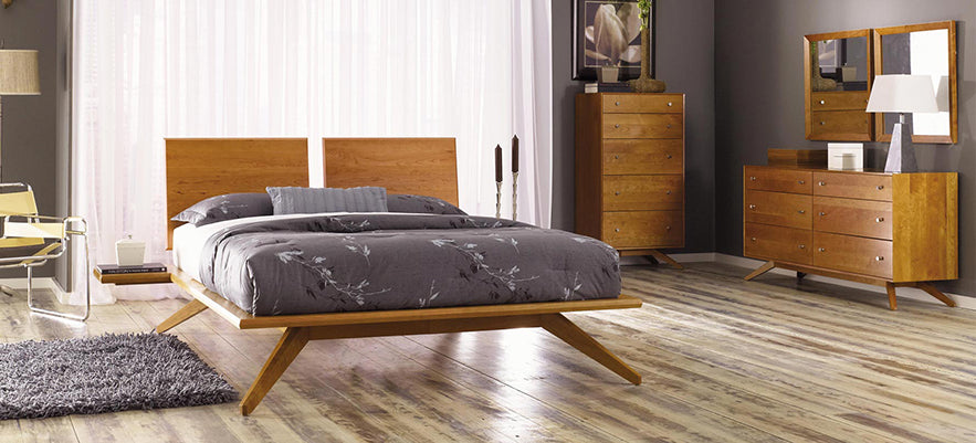 Wooden bed with gray bedding, accompanied by a matching dresser and tall chest.