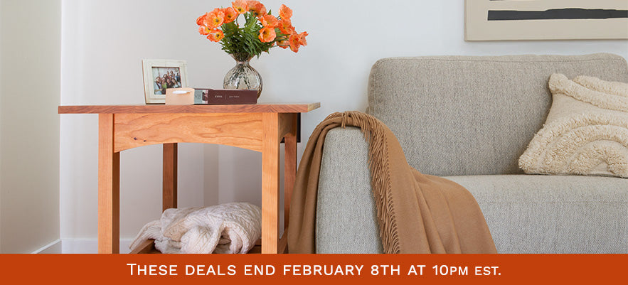 A wooden side table with a flower vase and a candle is next to a beige couch. The couch has a brown blanket draped over the arm and textured pillows. A text overlay at the bottom reads "These deals end February 8th at 10PM EST.