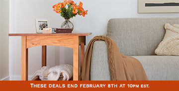 A small wooden side table with a vase of orange flowers, a photo frame, and a book sits beside a light gray sofa. A beige blanket is draped over the sofa's armrest. A red banner at the bottom reads, "These deals end February 8th at 10pm EST.