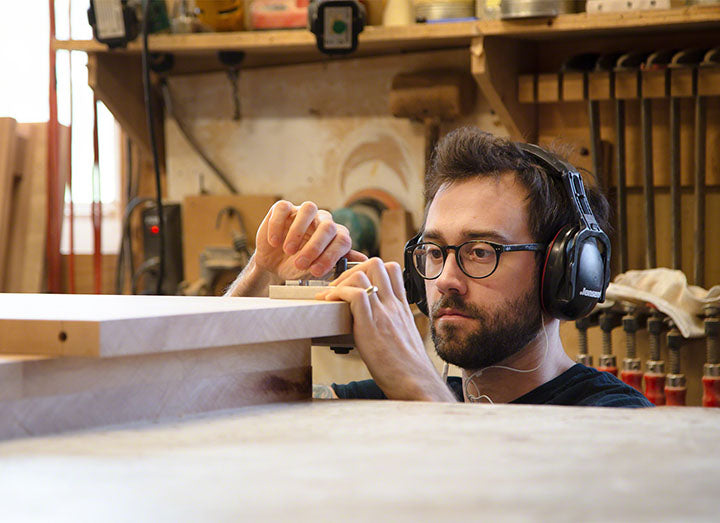 A man wearing headphones is working on a piece of wood.