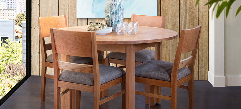 Round wooden dining table with four matching chairs featuring gray cushions.