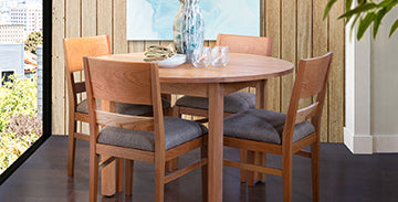 Round wooden dining table with four matching chairs featuring gray cushions.