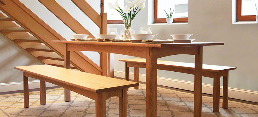 Wooden dining table with matching benches featuring white dishes and a vase of lilies.