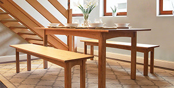 Wooden dining table with matching benches featuring white dishes and a vase of lilies.