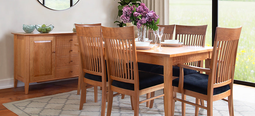 Wooden dining table for six with purple floral centerpiece.