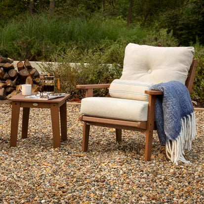 A wooden lounge chair and table in a gravel yard.