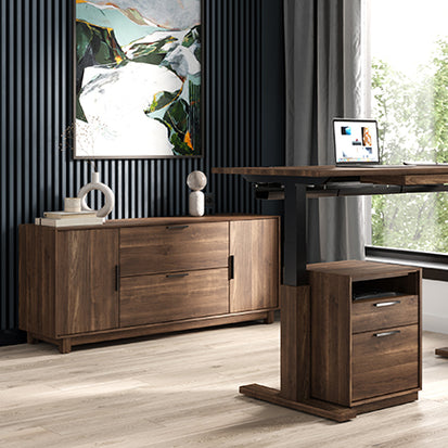 A home office with a dark accent wall featuring a colorful abstract painting. There is a wooden desk with an elevated section holding a laptop and a small cabinet underneath. Nearby, a wooden sideboard with decor items sits against the wall.