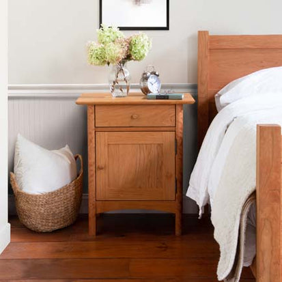 A wooden nightstand next to a bed in a bedroom.