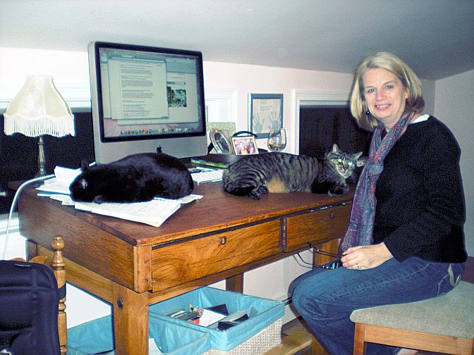 A woman sitting at a desk with two cats.
