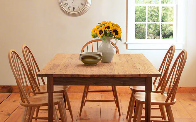 A wooden dining table with four chairs and a vase of sunflowers.
