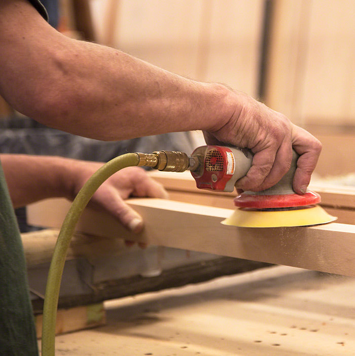 A man sanding a piece of wood with a sander.